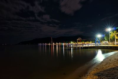 Illuminated pier over sea against sky at night