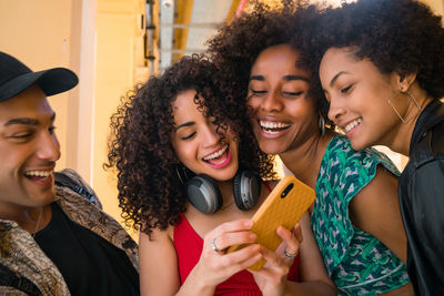 Happy young woman using phone by friends