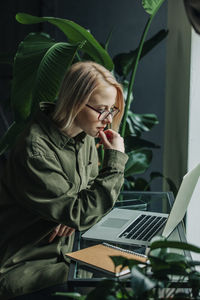 Businesswoman with hand on chin looking at laptop in home office