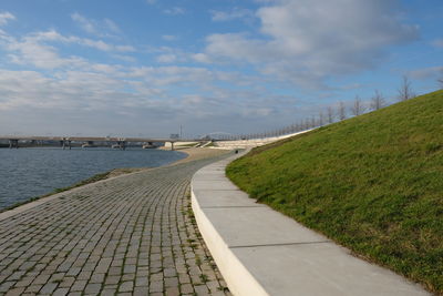 Empty footpath by road against sky