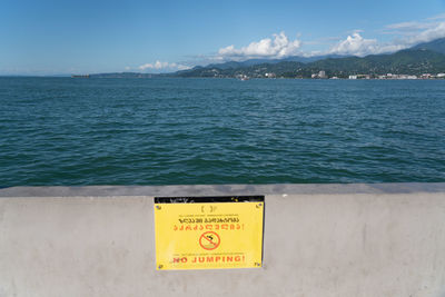 Information sign by sea against sky