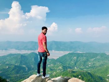 Young man standing on mountain against sky