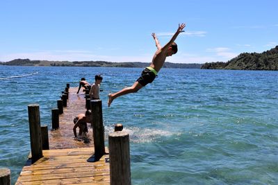 People jumping on pier over sea against sky