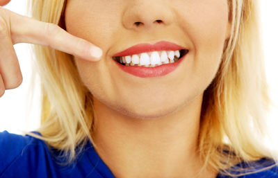 Midsection of young woman pointing at teeth against white background