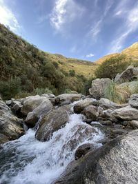 Scenic view of stream flowing through rocks against sky