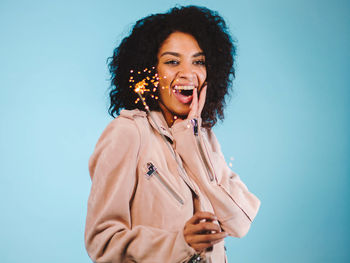 Cheerful young woman holding sparkler against blue background