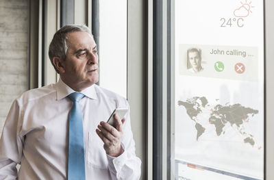 Businessman receiving a call on windowpane with world map in office