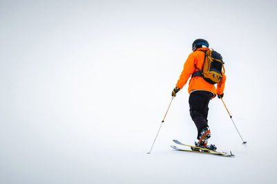 A male athlete in an orange jacket with a backpack on his shoulders and a helmet with a mask in a