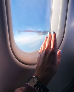 Cropped image of hand against sky seen through airplane window