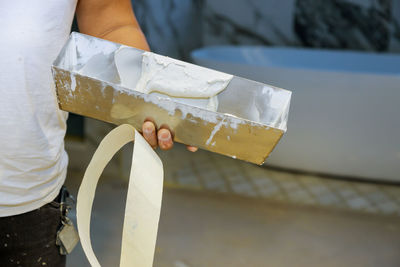 Midsection of mason holding plaster outdoors