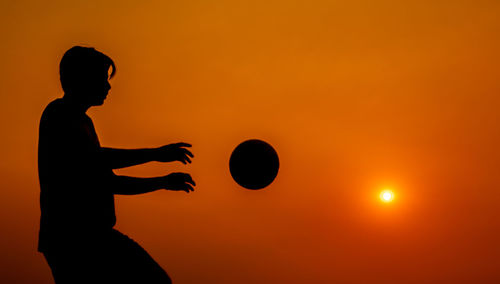 Silhouette man playing with ball against sky during sunset