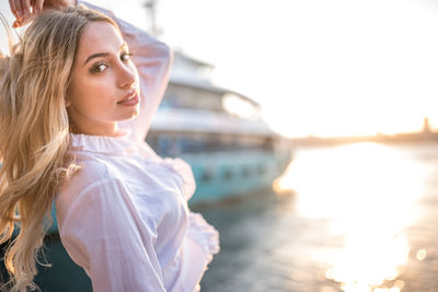 Portrait of beautiful woman standing against ship in river during sunset