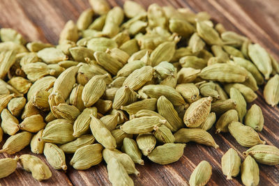 Green cardamom is scattered over vintage wood background