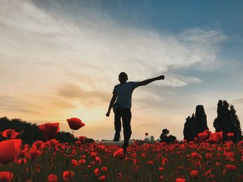 Low angle view of boy walking at poppy flower field against sky