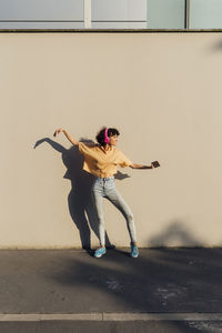 Young woman with headphones dancing in front of wall