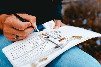 Midsection of woman painting on paper outdoors