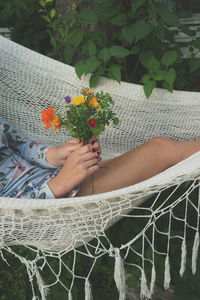 Midsection of woman holding flower bouquet while relaxing in hammock