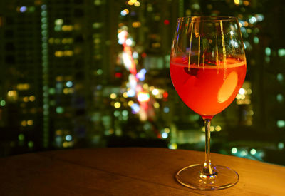 Glass of vivid red cocktail isolated on the rooftop terrace's table with blurry urban night view