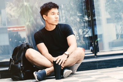 Young man looking away while sitting on window