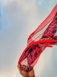 Close-up of hand holding red scarf blowing in the wind against cloudy blue sky.