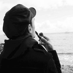 Rear view of man smoking with pipe against sea