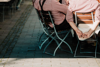 Midsection of friends sitting on chairs at sidewalk cafe