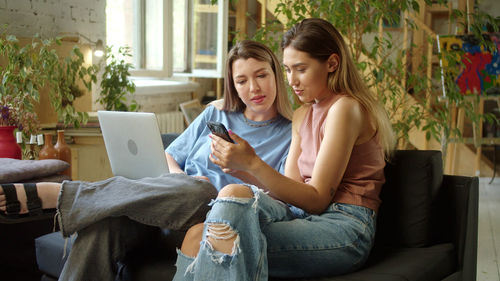 Friends using phone while sitting on sofa at home