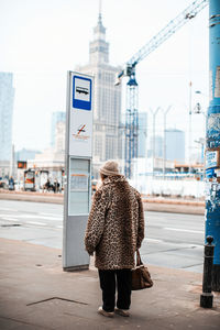 Rear view of woman standing ob footpath in city