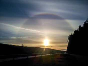 Road by silhouette trees against sky during sunset