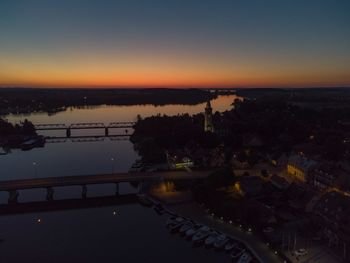 High angle view of river by illuminated city against sky during sunset