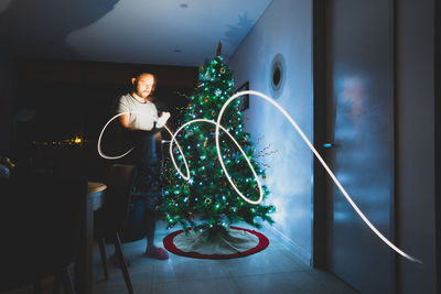 Woman holding illuminated christmas tree at home