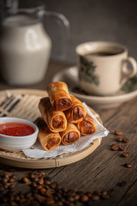 Fried spring rolls on a rattan plate with a sweet chilli sauce and a cup of coffee. malaysian snacks