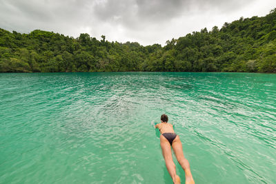 Rear view of woman wearing bikini diving in lake against forest