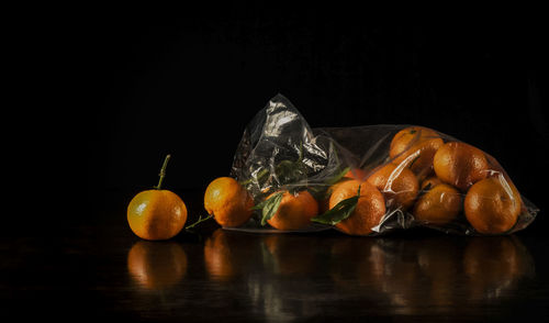 Still life of mandarins and leaves in plastic bag against black background