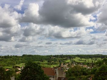 Trees on landscape against cloudy sky