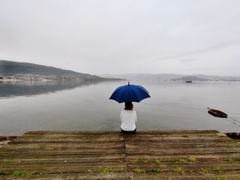Rear view of woman with umbrella on lake during rainy season
