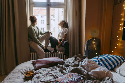 Young female friends sitting at window in bedroom