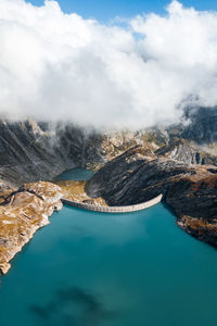 Aerial view of dam amidst mountains against cloudy sky