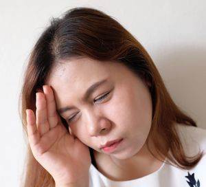 Young woman suffering from headache against white wall