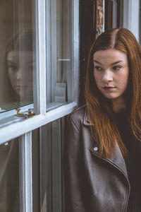 Portrait of young woman looking through window