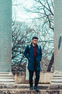 Portrait of young man standing against bare trees in winter