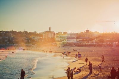 People on beach against clear sky during sunset