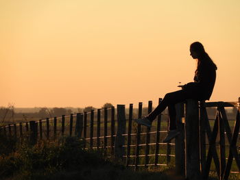 Side view of man standing by railing against sky during sunset