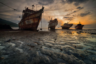 Nautical vessel on beach against sky during sunset