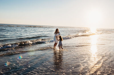 Couple standing on beach against clear sky during sunset