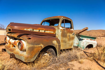 Abandoned vintage car on field against clear blue sky