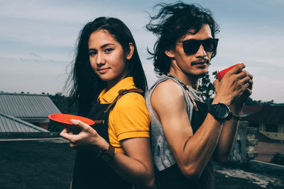 Portrait of young woman holding smart phone while standing against sky