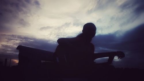 Silhouette man playing guitar against sky