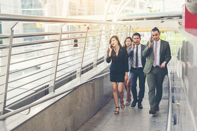 Colleagues using phones while walking on elevated walkway 