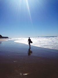 Silhouette man with surfboard walking on beach against clear sky